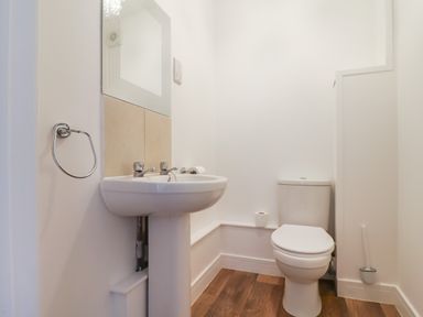 A bathroom with a pedestal sink a toilet a mirror and wooden flooring at Campion Cottage in Brendon Hill near Roadwater