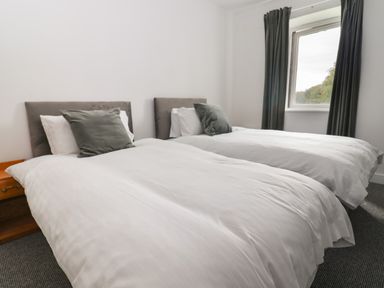 A bedroom with two single beds with white bedding and gray pillows near a window with dark curtains at Campion Cottage Brendon Hill near Roadwater