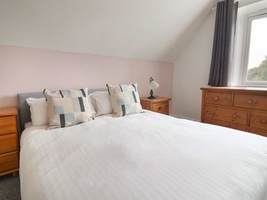 A bedroom with a double bed two bedside tables a lamp and a dresser by a window at Campion Cottage in Brendon Hill near Roadwater