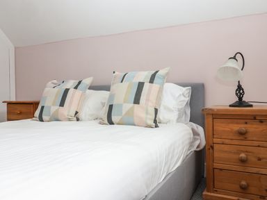 A bedroom with a bed with white sheets and two patterned pillows next to a wooden nightstand with a lamp at Campion Cottage in Brendon Hill near Roadwater