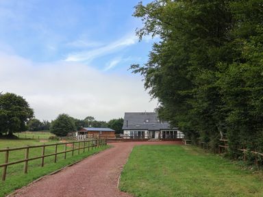 A country house with a driveway bordered by wooden fences and grassy areas with trees at Campion Cottage Brendon Hill near Roadwater