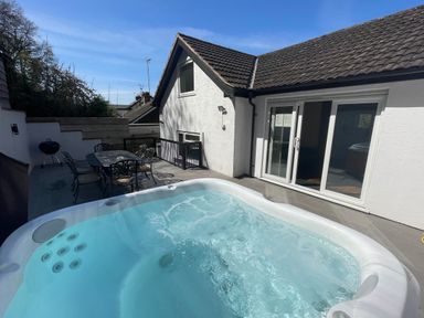 An outdoor patio area with a hot tub a metal table with six chairs and a barbecue grill at The Brambles in Monmouth