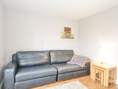A living room with a leather sofa a side table with a lamp and nested tables and a wall picture at The Brambles in Monmouth