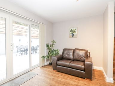 A room with a brown leather sofa plant and a painting next to glass sliding doors at The Brambles in Monmouth