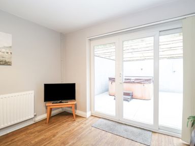 A room with wooden floor a small wooden table with a TV on it next to a radiator and sliding glass doors leading outside with a hot tub visible outside at The Brambles in Monmouth