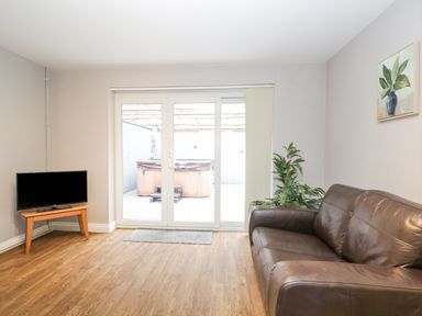 A living room with a brown leather sofa a small wooden table with a television a potted plant and a glass sliding door at The Brambles in Monmouth