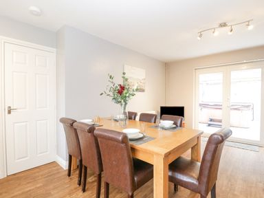 A dining room with a wooden table set with plates and bowls brown chairs and glass doors leading outside at The Brambles in Monmouth