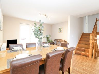 A dining room with a wooden table and brown chairs next to a living area and staircase at The Brambles in Monmouth