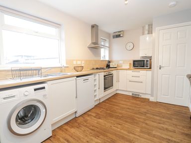 A kitchen with white cabinets washing machine dishwasher oven microwave and wooden floor at The Brambles in Monmouth