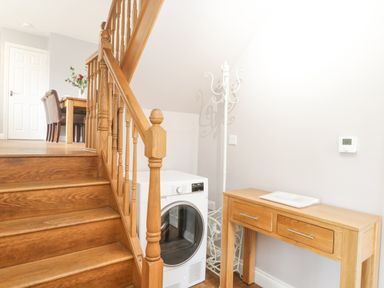 A staircase with wooden bannister next to a washing machine and a wooden table with drawers at The Brambles in Monmouth