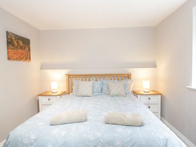 A bedroom with a double bed with blue floral bedding two rolled towels two bedside tables with lamps and a landscape painting on the wall at The Brambles in Monmouth
