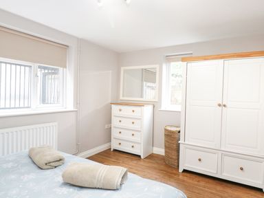 A bedroom with a bed and folded towels a white chest of drawers a mirror a white wardrobe and windows at The Brambles in Monmouth