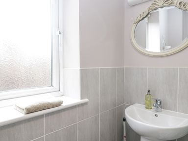 A bathroom corner with a frosted window, towel on the windowsill, a white sink with soap, and a decorative oval mirror