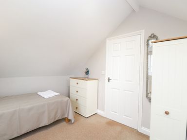 A bedroom with a single bed covered with a beige blanket a chest of drawers with a small round mirror a white door and a wardrobe with a mirror at The Brambles in Monmouth