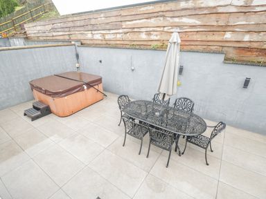An outdoor patio area with a hot tub and a metal dining table with six chairs and a closed umbrella at The Brambles in Monmouth