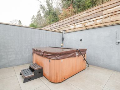 An outdoor hot tub with a cover and steps on a tiled patio surrounded by grey walls and a wooden fence at The Brambles in Monmouth