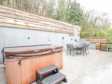 An outdoor patio area with a covered hot tub and a metal table with chairs and umbrella at The Brambles in Monmouth