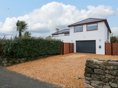 A modern two story house with a black garage door a gravel driveway and a hedge fence at Swyn Llyr in Rhosneigr