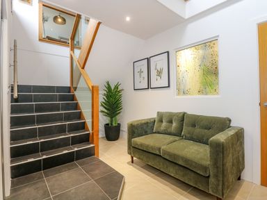 A staircase with black tiles next to a green sofa and potted plant with framed pictures on the wall at Swyn Llyr in Rhosneigr