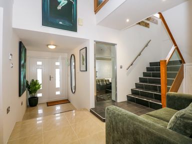 An entryway with a white front door a green plant a wall mirror and stairs next to a green sofa at Swyn Llyr in Rhosneigr