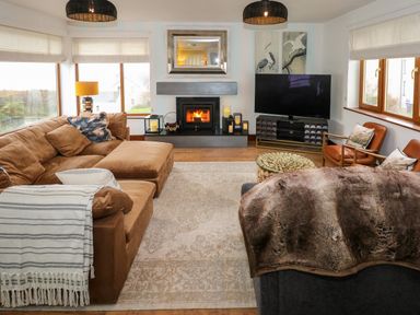 A living room with brown sofas a fireplace a television and large windows at Swyn Llyr in Rhosneigr