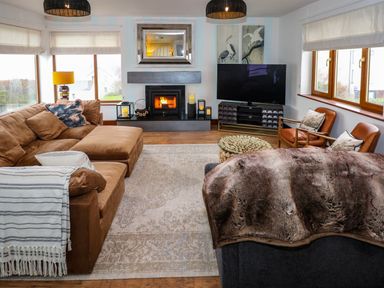A living room with a brown sectional sofa a fireplace a TV on a stand and two leather chairs at Swyn Llyr in Rhosneigr