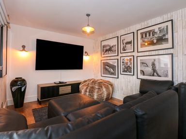 A living room with a black leather sofa a large flat screen tv a wooden cabinet black and white framed photos and a furry bean bag at Swyn Llyr in Rhosneigr