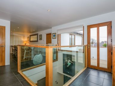 A hallway with glass and wood railing overlooking stairs stone tile floor and wooden door at Swyn Llyr in Rhosneigr