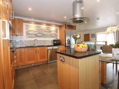 A kitchen with wooden cabinets an island with fruit bowl a stainless steel refrigerator and dishwasher at Swyn Llyr in Rhosneigr