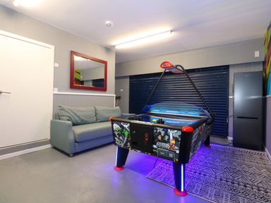 A room with a grey sofa an air hockey table a refrigerator and a wall mirror at Swyn Llyr in Rhosneigr