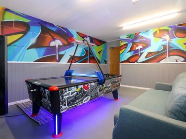 A game room with an air hockey table sofa and graffiti walls at Swyn Llyr in Rhosneigr