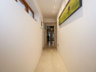 A narrow hallway with tiled floor and white walls decorated with framed pictures at Swyn Llyr in Rhosneigr