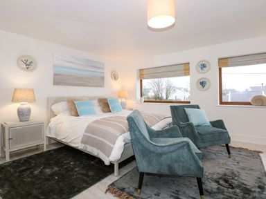 A bedroom with a double bed two armchairs bedside tables with lamps and artwork on the walls at Swyn Llyr in Rhosneigr