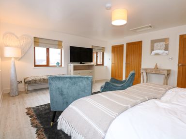 A bedroom with a bed a chair a bench a TV on a stand and wooden doors at Swyn Llyr in Rhosneigr
