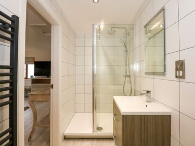 A bathroom with a shower, sink with cabinet, mirror, and towel radiator at Swyn Llyr in Rhosneigr