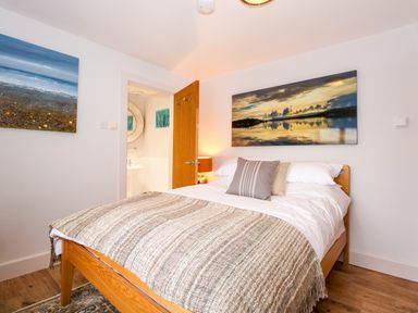A bedroom with a wooden bed a patterned throw pillows and landscape paintings at Swyn Llyr in Rhosneigr