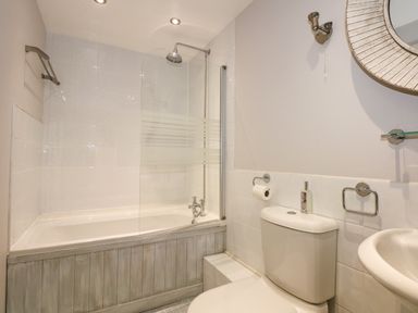 A bathroom with a bathtub shower combination a toilet a sink and a mirror at Swyn Llyr in Rhosneigr