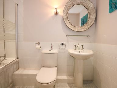 A bathroom with a toilet a sink a round mirror and a bathtub with a glass screen at Swyn Llyr in Rhosneigr