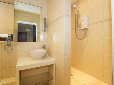 A bathroom with a sink and mirror and a shower area at Swyn Llyr in Rhosneigr