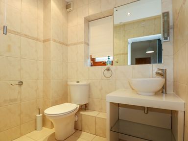 A bathroom with a toilet a sink with a faucet a large mirror and tiled walls at Swyn Llyr in Rhosneigr
