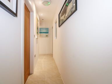 A narrow hallway with tiled floor white walls wooden door and framed pictures on the walls at Swyn Llyr in Rhosneigr