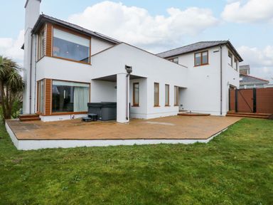 The exterior of a two story white house with large windows a patio and a grassy yard at Swyn Llyr in Rhosneigr