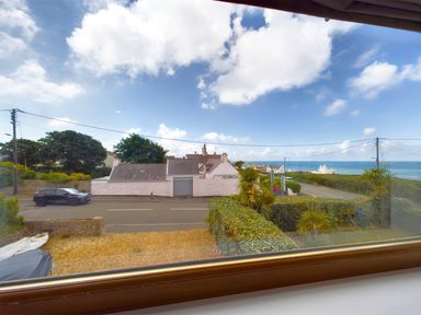 A window view showing a street with houses trees and the sea in the distance at Swyn Llyr in Rhosneigr