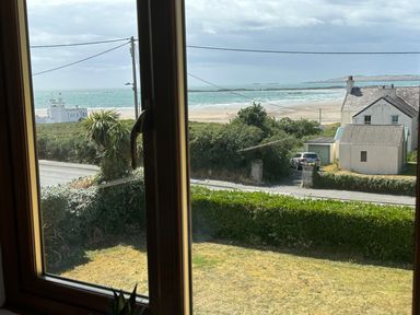 A window overlooking a garden hedge a road a house a beach and the sea at Swyn Llyr in Rhosneigr