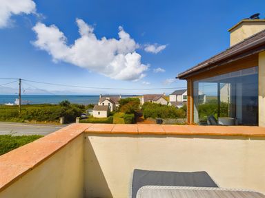 A view from a balcony showing houses gardens a road and sea under a blue sky at Swyn Llyr in Rhosneigr