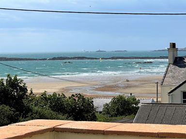 A view of the sea with small islands and a sandy beach with houses and greenery in the foreground at Swyn Llyr in Rhosneigr
