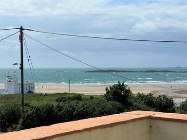 A view of the ocean with waves and a sandy beach from a balcony with a railing with a white building and power lines in the foreground at Swyn Llyr in Rhosneigr