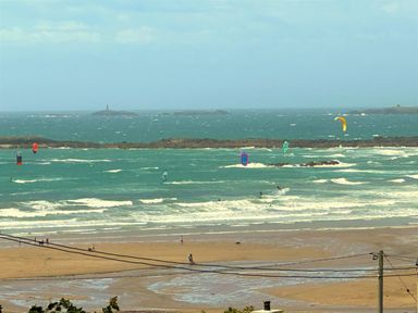 A beach with people walking and kite surfers on the water at Swyn Llyr in Rhosneigr