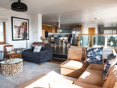 A living room with sofas and a glass-top coffee table connected to a kitchen with wooden cabinets and a dining table at Swyn Llyr in Rhosneigr