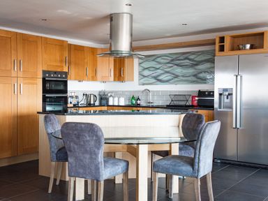 A kitchen with wooden cabinets a glass dining table with four chairs a stainless steel refrigerator and an oven at Swyn Llyr in Rhosneigr